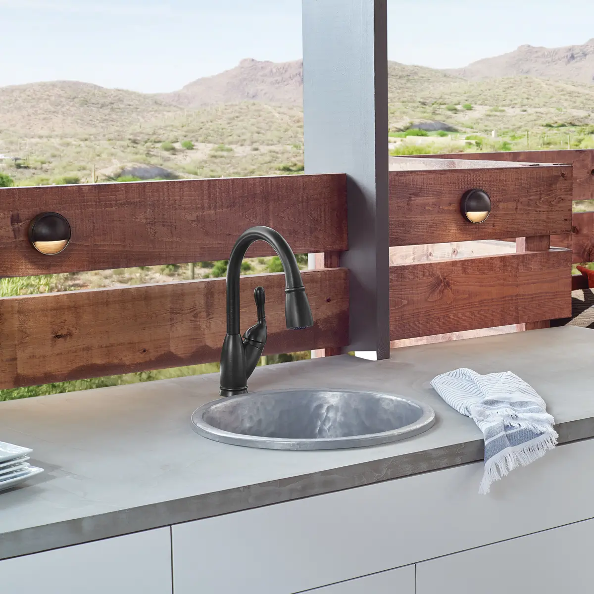 Outdoor kitchen counter with integrated deck lights on a wooden fence at dusk